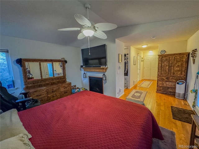 bedroom with lofted ceiling, light wood-style floors, a fireplace, baseboards, and ceiling fan