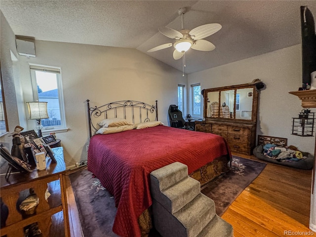 bedroom featuring ceiling fan, vaulted ceiling, wood finished floors, and a textured ceiling