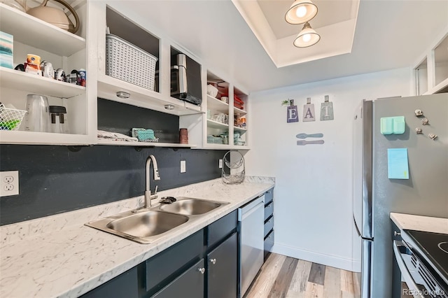 kitchen featuring sink, appliances with stainless steel finishes, light stone counters, light hardwood / wood-style floors, and a raised ceiling