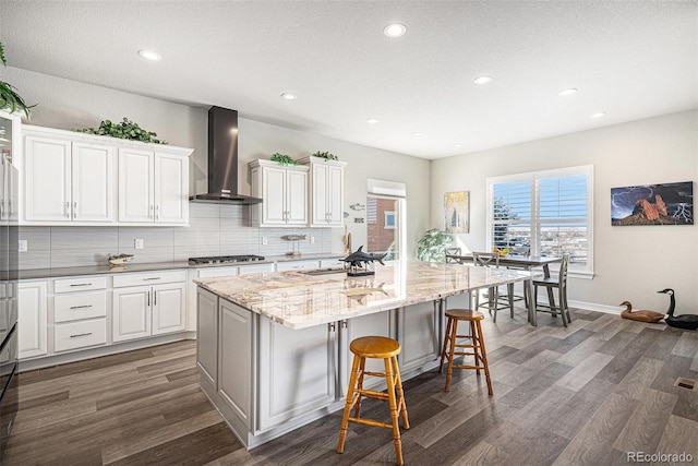 kitchen featuring a breakfast bar, a sink, tasteful backsplash, wall chimney range hood, and dark wood-style flooring