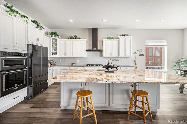 kitchen with black appliances, dark wood-style floors, a breakfast bar area, white cabinets, and wall chimney range hood