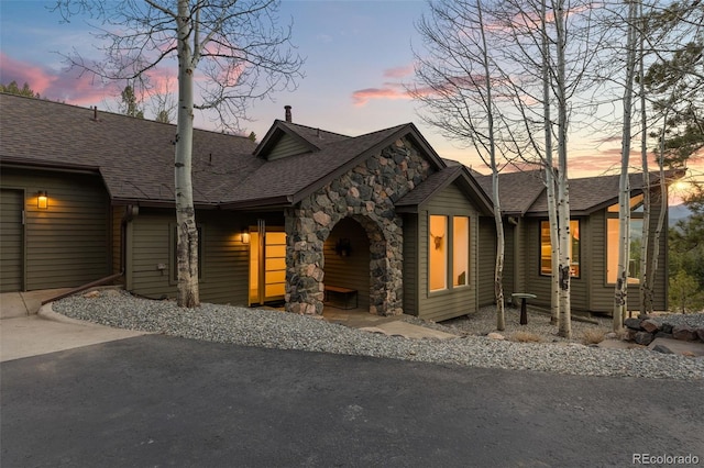 view of front of house with stone siding, a shingled roof, and driveway