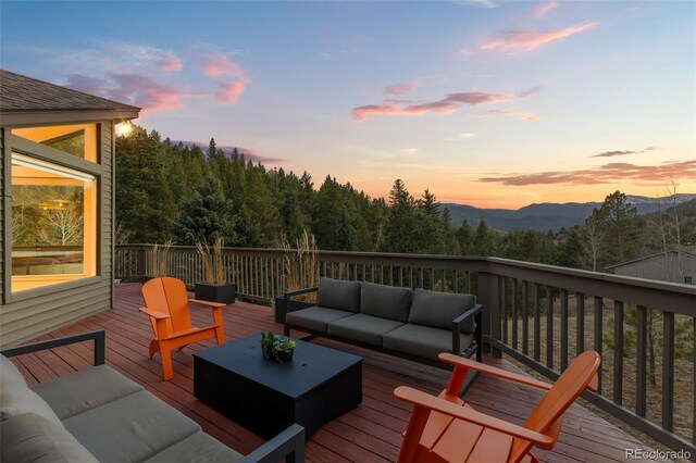 deck at dusk with a wooded view and outdoor lounge area