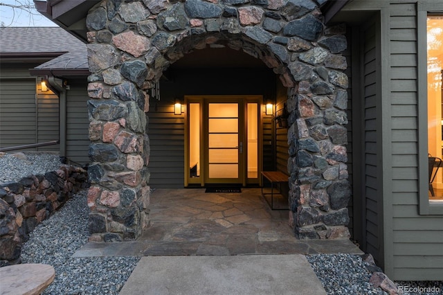 property entrance featuring a shingled roof and stone siding