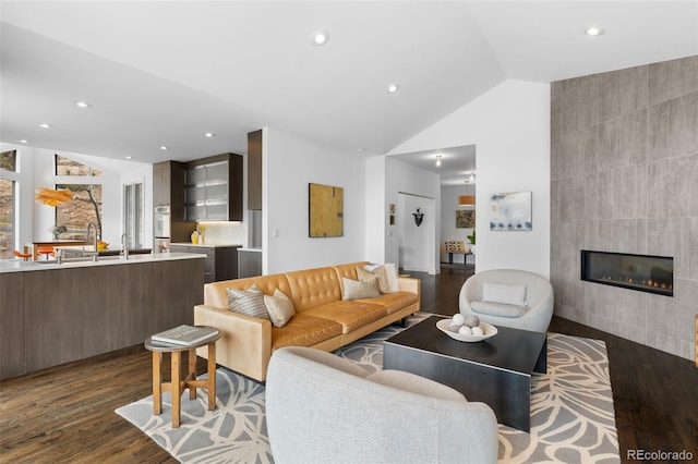 living area with lofted ceiling, dark wood-style floors, a tile fireplace, and recessed lighting