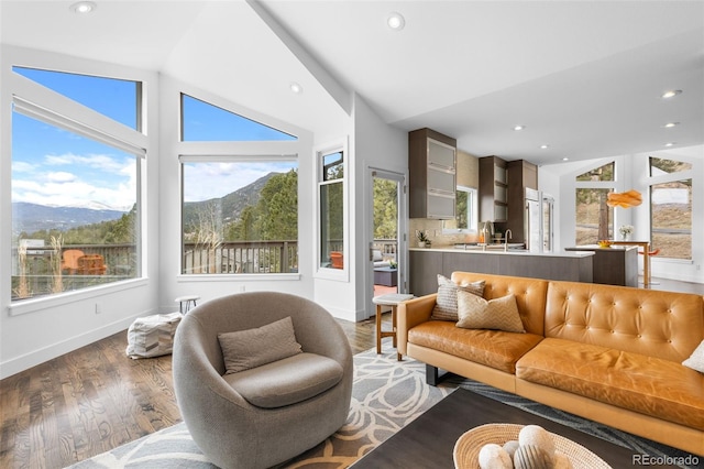 living area with vaulted ceiling, wood finished floors, recessed lighting, baseboards, and a mountain view