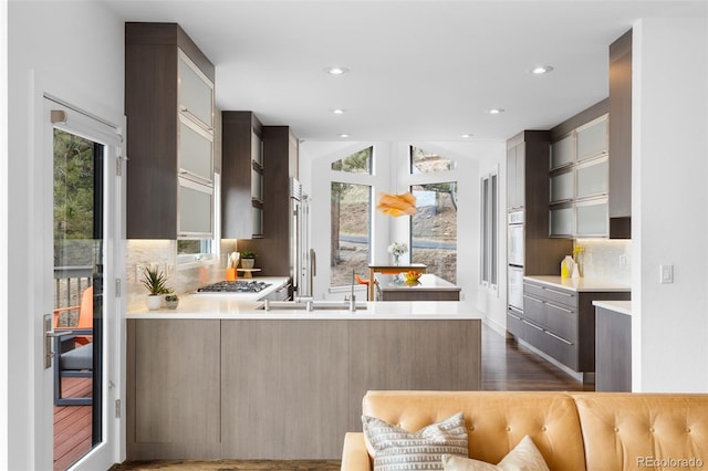 kitchen with light countertops, a peninsula, glass insert cabinets, and decorative backsplash