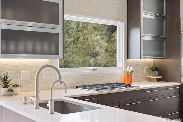 kitchen with light countertops, tasteful backsplash, stainless steel gas cooktop, modern cabinets, and dark brown cabinets