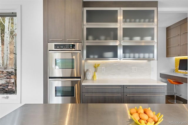 kitchen with modern cabinets, glass insert cabinets, double oven, and backsplash
