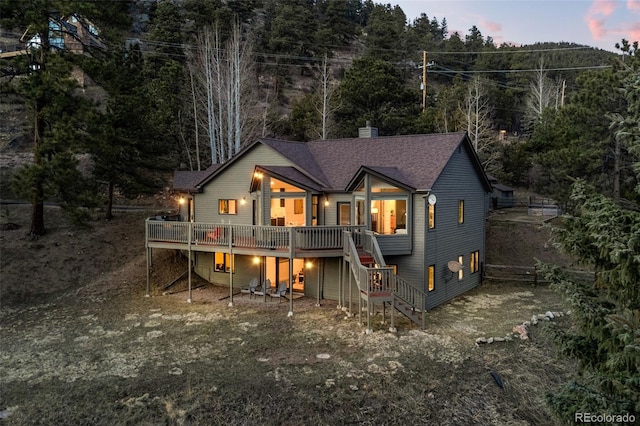 back of property at dusk featuring stairs, a chimney, roof with shingles, and a deck