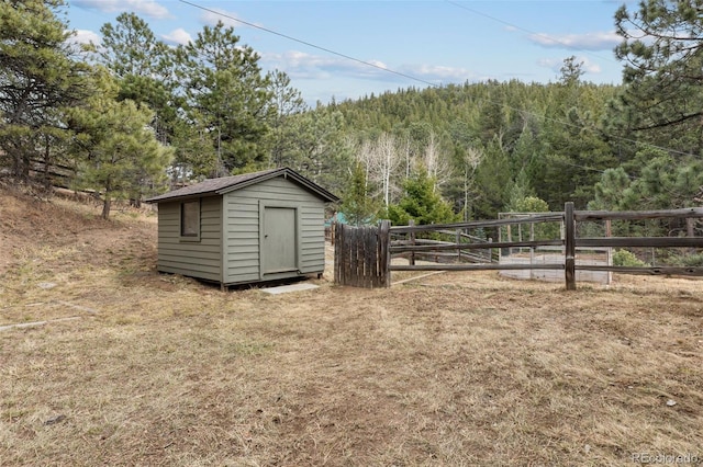 view of yard with an outdoor structure, fence, a forest view, and a storage shed