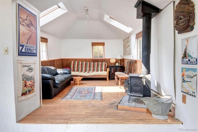 living room with lofted ceiling with skylight, wainscoting, a wood stove, and a wealth of natural light