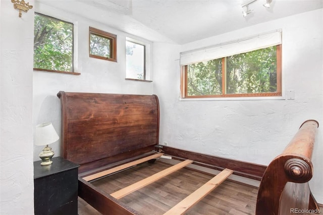 bedroom featuring a textured wall, rail lighting, baseboards, and wood finished floors