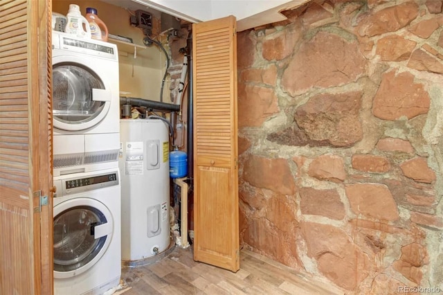 clothes washing area featuring stacked washer and dryer, wood finished floors, water heater, and laundry area