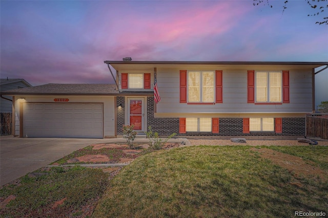 split level home featuring an attached garage, a yard, driveway, and brick siding