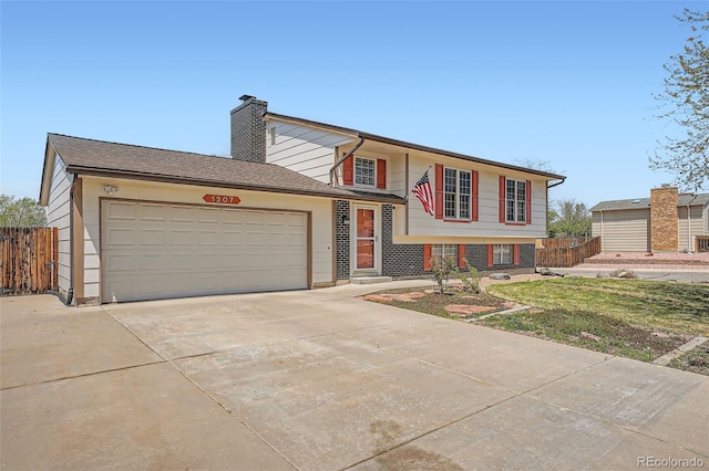 split level home with fence, an attached garage, a chimney, and driveway