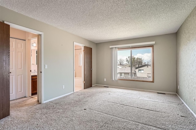 unfurnished bedroom with ensuite bathroom, a textured ceiling, carpet, and visible vents