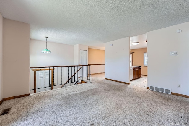 unfurnished room with light colored carpet, baseboards, visible vents, and a textured ceiling