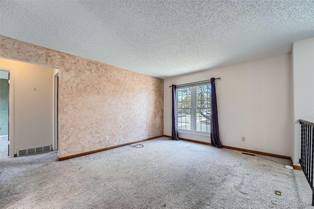 spare room with a textured ceiling, visible vents, and carpet