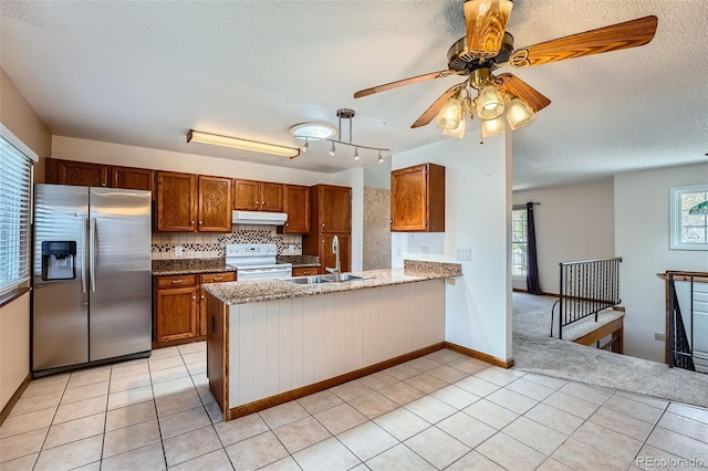 kitchen featuring white electric range oven, stainless steel fridge, under cabinet range hood, brown cabinets, and a sink