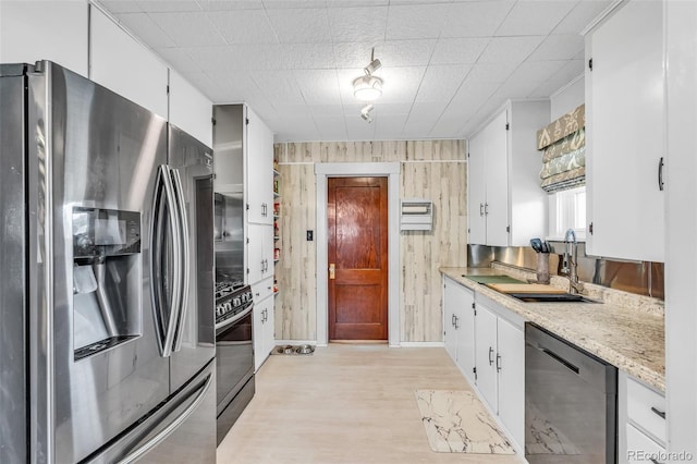 kitchen featuring white cabinetry, sink, wood walls, appliances with stainless steel finishes, and light wood-type flooring