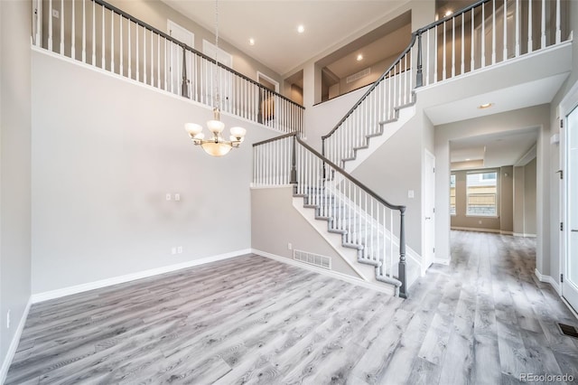 foyer entrance featuring wood finished floors, stairs, a high ceiling, a chandelier, and baseboards