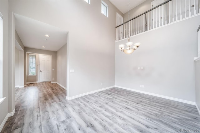 foyer with healthy amount of natural light, wood finished floors, a chandelier, baseboards, and a towering ceiling