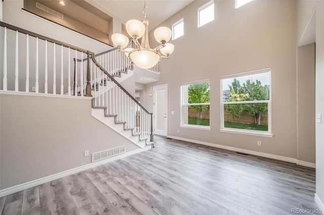 foyer featuring a high ceiling, wood finished floors, a chandelier, stairs, and baseboards
