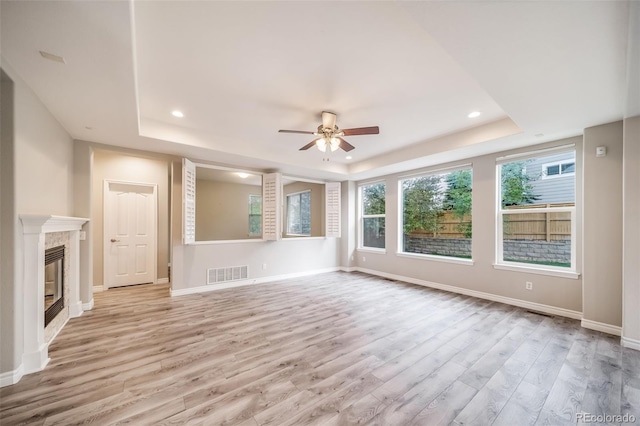 unfurnished living room with a raised ceiling, a ceiling fan, wood finished floors, healthy amount of natural light, and recessed lighting