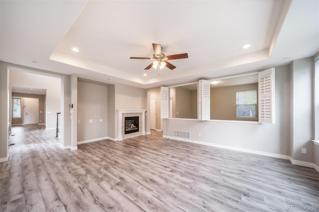 unfurnished living room featuring a tray ceiling, recessed lighting, ceiling fan, wood finished floors, and plenty of natural light