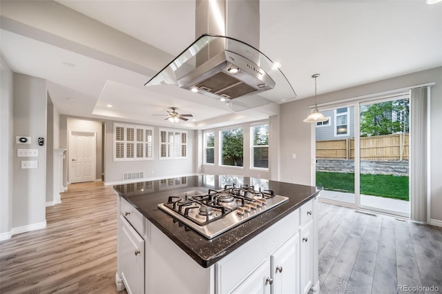 kitchen with stainless steel gas cooktop, island range hood, light wood-type flooring, white cabinetry, and baseboards