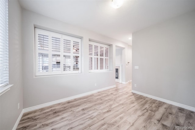 unfurnished room featuring light wood finished floors, plenty of natural light, and baseboards