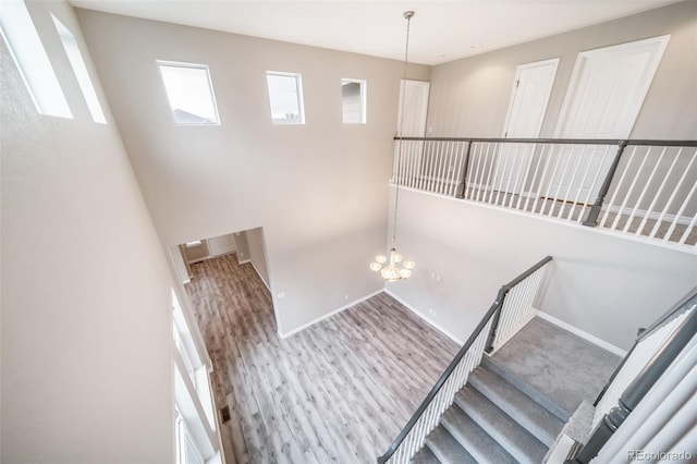 stairway featuring plenty of natural light, baseboards, wood finished floors, and a chandelier