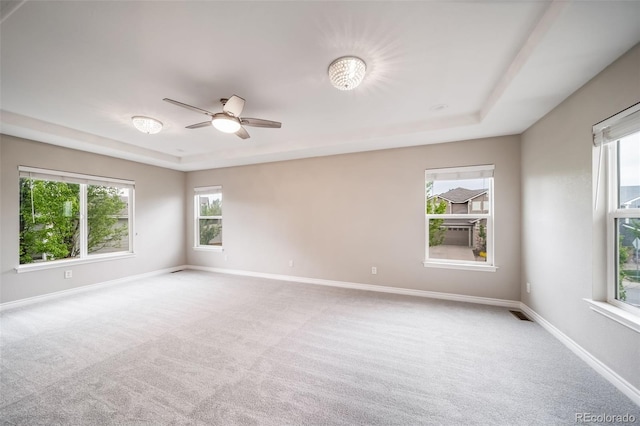 carpeted empty room featuring a raised ceiling, ceiling fan, and baseboards