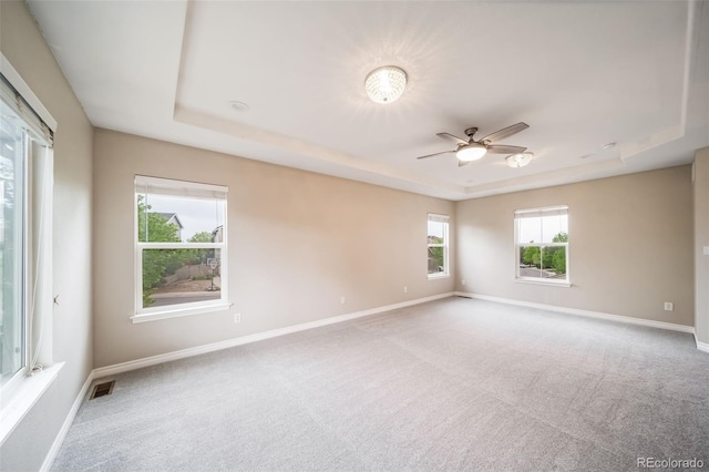 carpeted spare room with a tray ceiling, ceiling fan, and baseboards