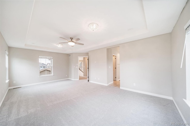 empty room with a tray ceiling, light carpet, and baseboards