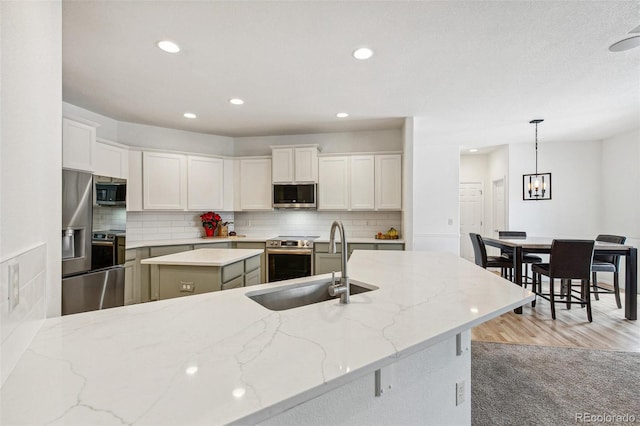 kitchen featuring hanging light fixtures, stainless steel appliances, white cabinets, and a kitchen island with sink