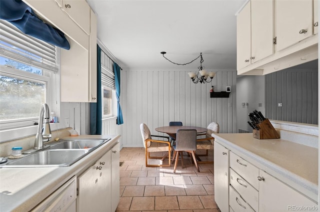 kitchen featuring dishwasher, an inviting chandelier, light countertops, white cabinetry, and a sink