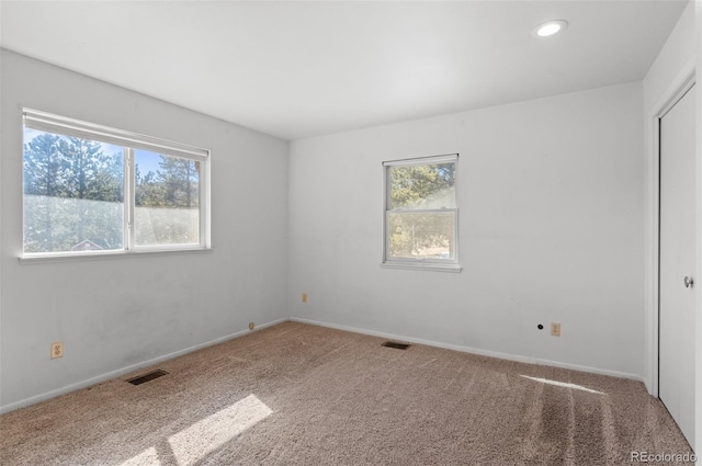 carpeted spare room featuring baseboards, visible vents, and a healthy amount of sunlight