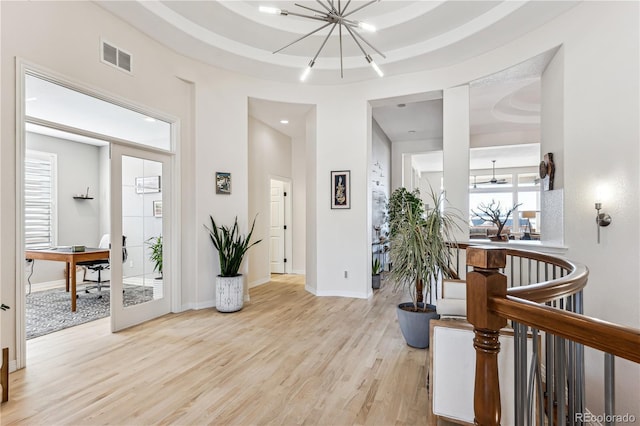 foyer entrance with light wood-type flooring, an inviting chandelier, and a raised ceiling