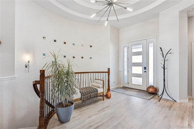 foyer with a raised ceiling, a chandelier, and light wood-type flooring