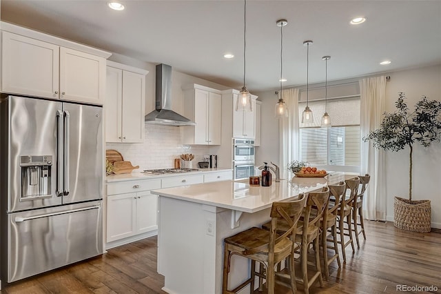 kitchen with white cabinets, wall chimney exhaust hood, a kitchen island with sink, and appliances with stainless steel finishes