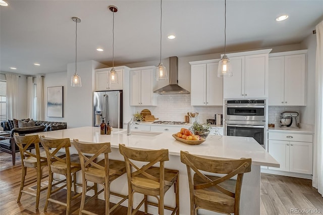 kitchen featuring white cabinets, wall chimney exhaust hood, decorative light fixtures, and appliances with stainless steel finishes