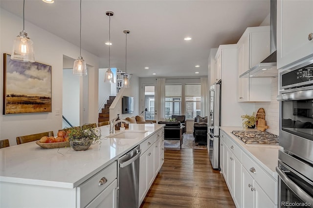 kitchen with appliances with stainless steel finishes, sink, pendant lighting, white cabinetry, and an island with sink