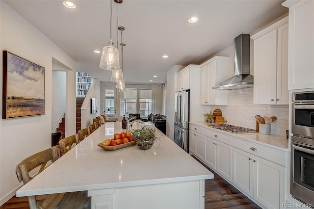 kitchen featuring appliances with stainless steel finishes, wall chimney range hood, an island with sink, and a breakfast bar area