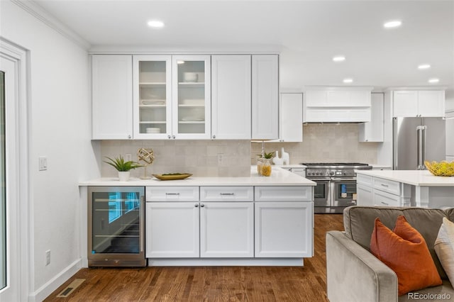 kitchen with high quality appliances, white cabinetry, dark hardwood / wood-style floors, and beverage cooler