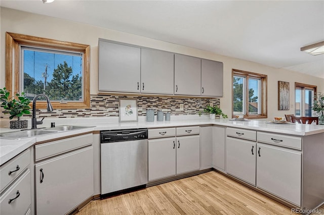 kitchen featuring kitchen peninsula, sink, light hardwood / wood-style flooring, stainless steel dishwasher, and tasteful backsplash