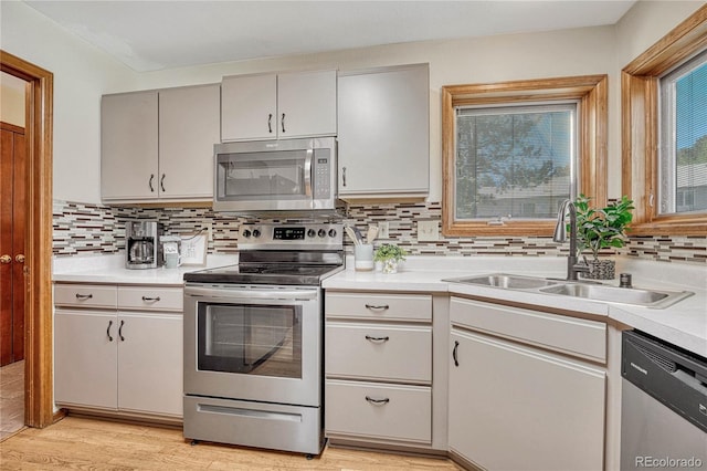 kitchen featuring stainless steel appliances, light wood-type flooring, decorative backsplash, and sink