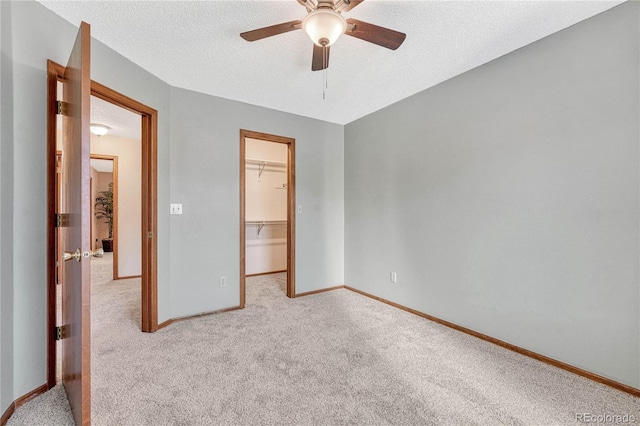 unfurnished bedroom with a textured ceiling, light carpet, ceiling fan, a closet, and a walk in closet