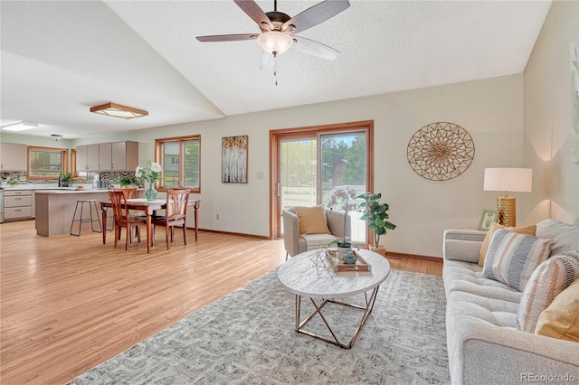 living room with vaulted ceiling, a textured ceiling, ceiling fan, and light hardwood / wood-style floors